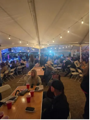 Guests seated at long tables under string lights in the tent.